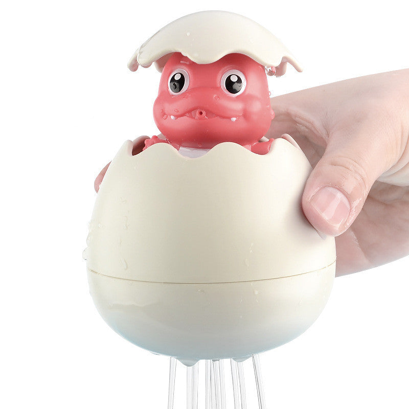 Baby holding water-spraying dinosaur egg bath toy